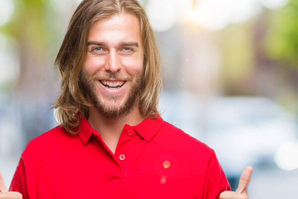 Young handsome man with long hair over isolated background success sign doing positive gesture with hand, thumbs up smiling and happy. Looking at the camera with cheerful expression, winner gesture.