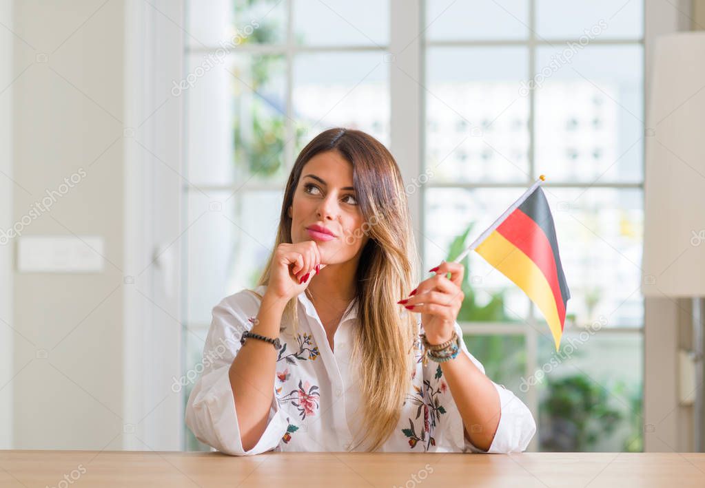 Young woman at home holding flag of Germany serious face thinking about question, very confused idea