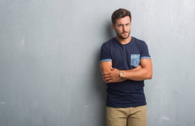 Gri grunge duvar şüpheci ve sinir, onaylamayan ifade yüz çapraz kollu yakışıklı genç adam. Negatif kişi.