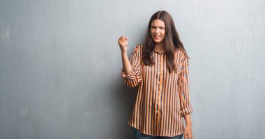 Grunge gri duvar öfkeli ve sinirli sinirli ve öfke ile bağırarak süre öfkeli yumruk yükselterek genç esmer kadın. Öfke ve agresif kavramı.