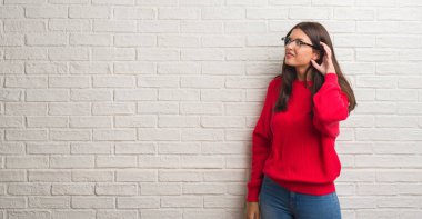 Bir işitme söylenti ya da dedikodu için dinleme kulak üzerinde el ile gülümseyen beyaz tuğla duvarın üzerinden duran genç esmer kadın. Sağırlık kavramı.