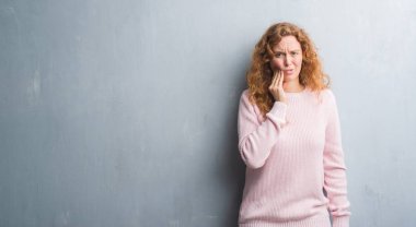 Genç redhead gri grunge duvar giyen üzerinde pembe kadın kazak diş ağrısı veya dişlerde dişlerle ilgili hastalık nedeniyle ağız acı ifadesi ile el ile dokunmak. Diş hekimi kavramı.