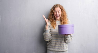 Gri grunge duvar kutusu çok mutlu ve heyecanlı, kazanan ifadesi ile çığlık zaferini kutluyor büyük tutan genç Kızıl saçlı kadın gülümse ve el kaldırdı