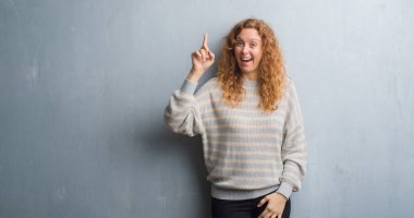 Gri grunge duvar işaret parmağı kadar başarılı fikir genç Kızıl saçlı kadın. Çıktıktan ve mutlu. Bir numara.