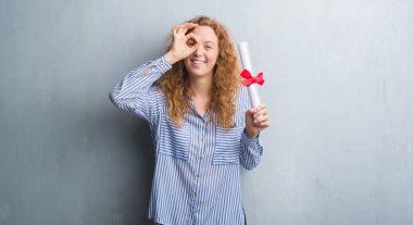 Genç redhead iş kadını mutlu yüz el parmaklarının arasından seyir göz üzerinde ok işaretiyle yapıyor gülümseyen ile diploma tutan gri grunge duvarın üzerinden
