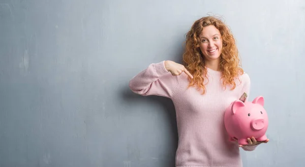 Jonge Roodharige Vrouw Grijs Grunge Muur Holding Piggy Bank Dollar — Stockfoto