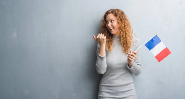 Giovane Donna Rossa Sopra Grigio Grunge Muro Che Tiene Bandiera — Foto Stock