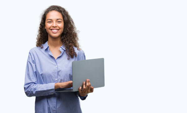Young hispanic woman holding computer laptop with a happy face standing and smiling with a confident smile showing teeth