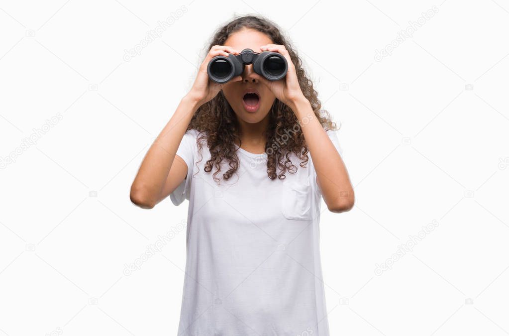 Young hispanic woman looking through binoculars scared in shock with a surprise face, afraid and excited with fear expression
