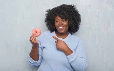 Pembe çörek el ve parmak ile işaret çok mutlu yemek gri grunge duvarın üzerinden genç Afro-Amerikan kadın