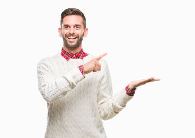 Hayret ve el ile sunulması ve parmak ile işaret ederken kameraya gülümseyen izole arka plan üzerinde kış kazak giyen genç yakışıklı adam.