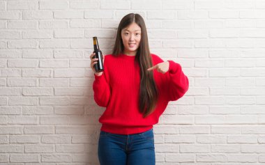 Sürpriz yüz işaret parmağı kendine bira içme tuğla duvarın üzerinden Genç Çinli kadın