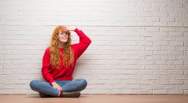 Tuğla duvardan çok mutlu ve gülümseyen uzakta el ile üzerine kafa seyir oturan genç Kızıl saçlı kadın. Arama kavramı.