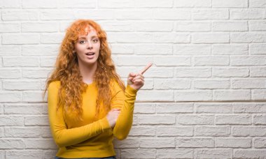 Tuğla duvar el ve parmak ile tarafına işaret çok mutlu üzerinde duran genç Kızıl saçlı kadın