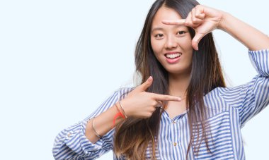 Genç Asyalı kadın elle yapma çerçeve ve parmakları ile mutlu yüz gülümseyen izole arka plan üzerinde. Yaratıcılık ve Fotoğrafçılık kavramı.