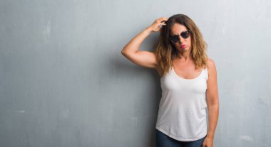 Orta yaş İspanyol kadın güneş gözlüğü takıyor gri duvar yüzünden yanıltır ve soru hakkında merak ediyorum. Şüphe, kafasına el ile düşünme ile belirsiz. Dalgın kavramı.