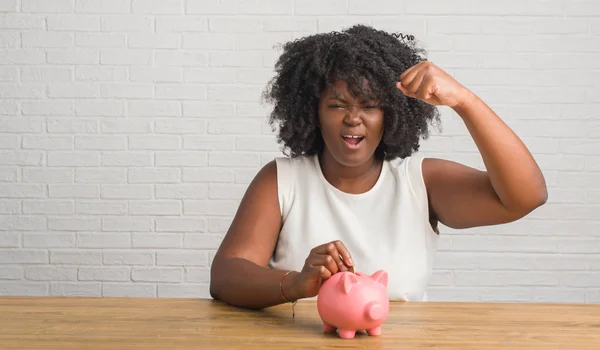 Unga Afroamerikanska Kvinnan Sitter Bord Innehav Piggy Bank Irriterad Och — Stockfoto