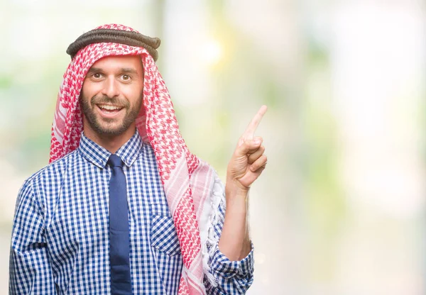 若いハンサムなアラビアン ビジネス男の顔に大きな笑みを浮かべて隔離された背景にクーフィーヤを着てカメラを見て側の手と指で指す — ストック写真