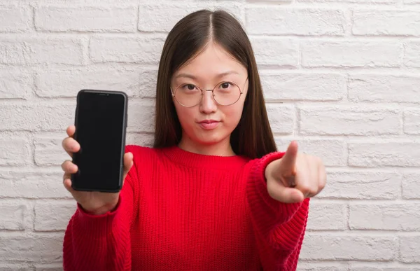 Jovem Chinesa Sobre Parede Tijolo Mostrando Smartphone Apontando Com Dedo — Fotografia de Stock