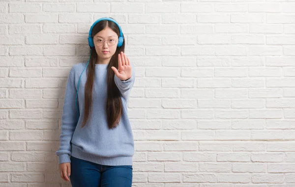 Mladá Číňanka Cihlová Zeď Nošení Sluchátek Otevřenou Rukou Dělá Stopku — Stock fotografie