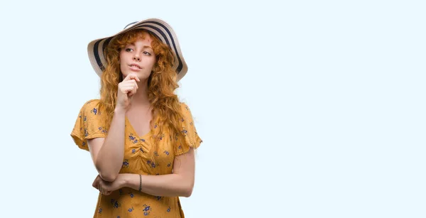 年轻的红头发的女人戴着夏天的帽子和衣着严肃的面孔思考问题 非常困惑的想法 — 图库照片