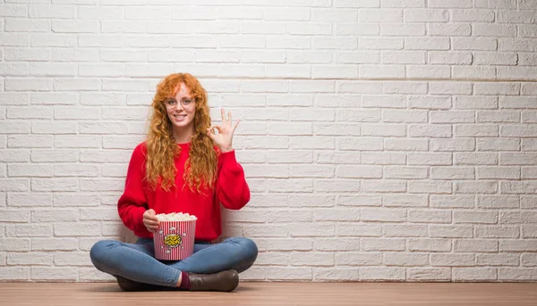 Joven Pelirroja Sentada Sobre Pared Ladrillo Comiendo Palomitas Haciendo Signo — Foto de Stock