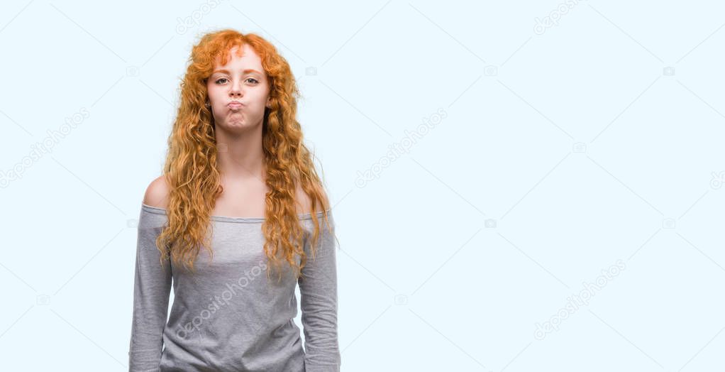 Young redhead woman puffing cheeks with funny face. Mouth inflated with air, crazy expression.