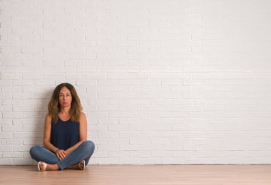 Orta yaş İspanyol kadın beyaz tuğla duvarın üzerinden katta oturan depresif ve kızgın ve korkmuş ağlıyor sıkıntı için endişeleniyorum. Üzgün ifade.