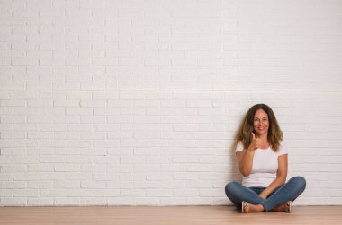 Orta yaş İspanyol kadın beyaz tuğla duvar mutlu ok işareti, başparmak ile parmak, mükemmel işareti yapıyor kocaman bir gülümseme ile