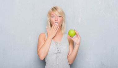 Hata, korku, sessizlik içinde gizli kavramı korkmuş ifade için utanç ile yetişkin beyaz kadın el ile yeşil elma kapak ağız yeme grunge gri duvar yüzünden şok