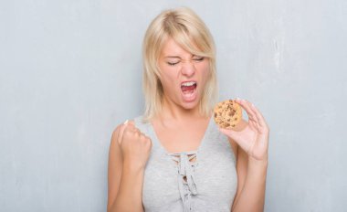 Gri grunge beyaz yetişkin kadın duvar çikolata bisküvi rahatsız yeme ve boşa çıkarmak ile öfke, çılgın ve yükseltilmiş eliyle diye bağıran öfke kavramı bağırarak.