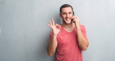 Parmak, mükemmel sembolü ile ok işareti yapıyor telefonda konuşurken gri grunge duvarın üzerinden beyaz delikanlı