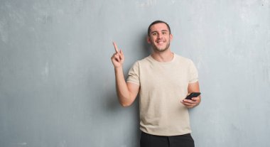 Gri grunge üzerinde beyaz delikanlı duvar manifatura smartphone el ve parmak ile tarafına işaret çok mutlu kullanarak bir ileti