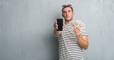 Dolar ve smarphone tutan gri grunge duvarın üzerinden beyaz delikanlı 