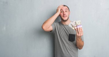 Genç beyaz adam baş, el ile vurguladı paralarını tutan gri grunge duvarın üzerinden şok utanç ve sürpriz suratla, öfkeli ve sinirli. Korku ve hata için üzgün.