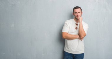 Beyaz delikanlı emin çapraz kollar ve çeneme kaldırdı el ile gülümseme ile kameraya bakarak güneş gözlüğü takıyor gri grunge duvarın üzerinden. Pozitif düşünce.