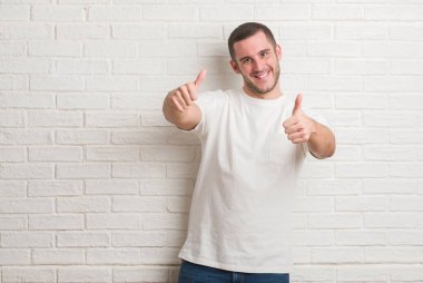 Beyaz tuğla duvar gülümseyen ve süre seyir ve kamera boyutu işaret parmaklarıyla yapıyor el ile kendinden emin eller üzerinde duran beyaz delikanlı. Ölçü kavramı.