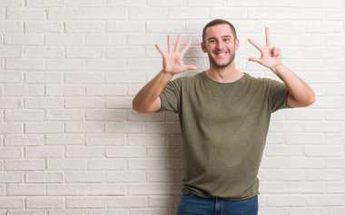 Beyaz delikanlı gösterilen ve parmakları ile işaret beyaz tuğla duvarın üzerinden ayakta sekiz kendinden emin ve mutlu gülümseyerek iken numara.