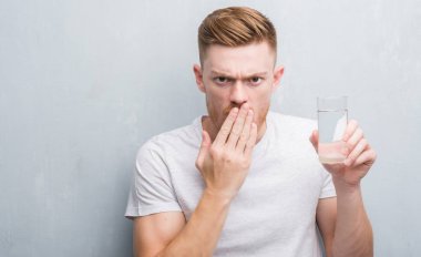 Sessizlik, gizli kavramı gri grunge duvar içme suyu kapak ağız el için hata, ifade korku, utanç ile şok ile genç Kızıl saçlı adam korkuttu