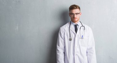 Young redhead doctor man over grey grunge wall with a confident expression on smart face thinking serious clipart