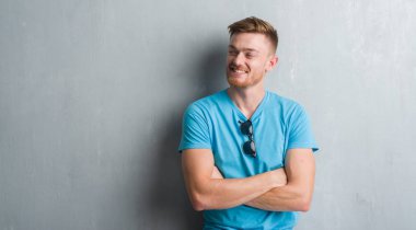 Gri grunge duvar görünümlü yan ve dik dik bakma uzağa düşünce gülümseyen gündelik kıyafeti giymiş genç Kızıl saçlı adam.