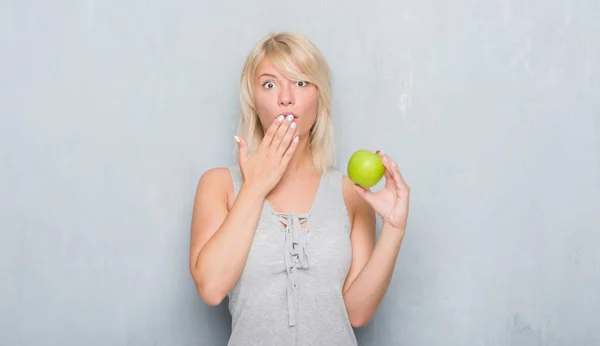 成年白种女人在垃圾灰墙上吃绿色苹果捂着嘴用手震惊的错误 表达恐惧 害怕沉默 秘密概念 — 图库照片