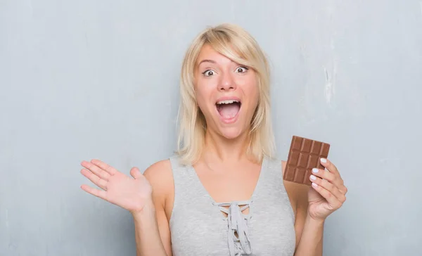 非常に幸せと興奮 勝者式笑顔で叫んで勝利を祝ってと手を上げたチョコレートバーを灰色のグランジの壁を食べる以上の白人成人女性 — ストック写真