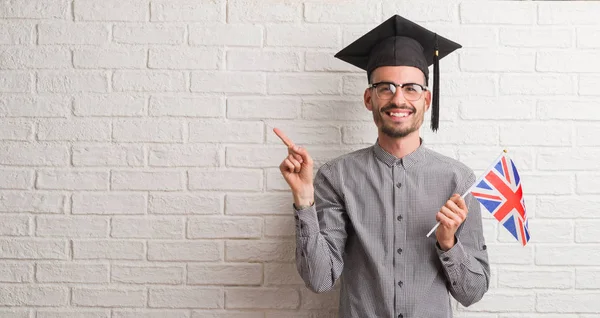 Homem Adulto Jovem Sobre Parede Tijolo Usando Tampa Graduação Segurando — Fotografia de Stock