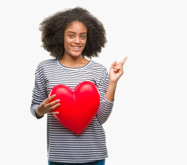 年轻的美国黑人妇女举行红色心脏在爱在隔绝的背景非常愉快指向用手和手指到边 — 图库照片