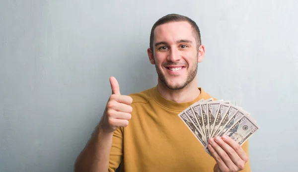 Young Caucasian Man Grey Grunge Wall Holding Dollars Happy Big — Stock Photo, Image