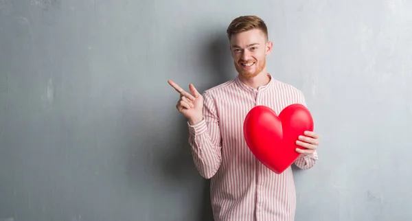 Young Redhead Man Grey Grunge Wall Holding Red Heart Very — Stock Photo, Image