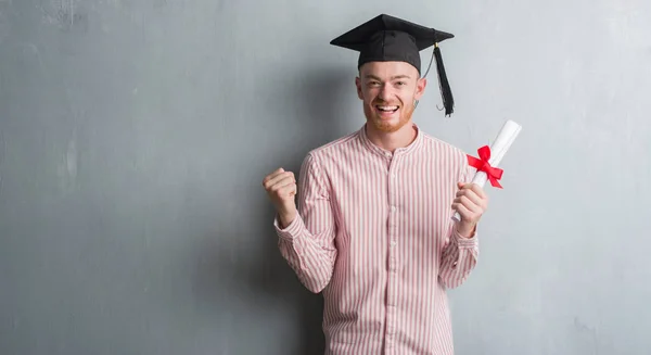 赤毛の若い男誇りに思って叫んでと勝利と非常に興奮して 成功を祝っての学位を保持大学院帽をかぶってグレー グランジ壁を越えて感情を応援 — ストック写真