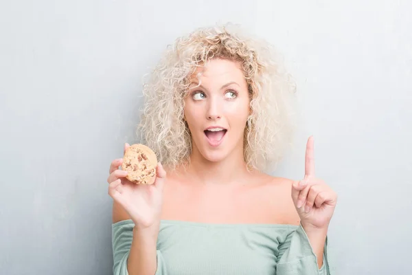 Young Blonde Woman Grunge Grey Wall Eating Chocolate Chip Cooky — Stock Photo, Image