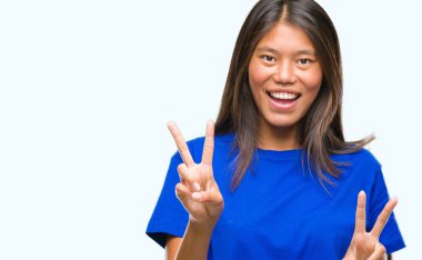 Genç Asyalı kadın parmaklarını zafer işareti yaparken gösterilen kamera seyir gülümseyen izole arka plan üzerinde. İki numaralı.